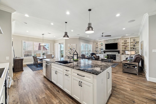 kitchen with ceiling fan, dark stone counters, a fireplace, dark wood-style floors, and a sink