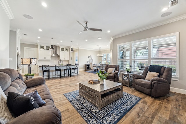 living room with baseboards, visible vents, recessed lighting, crown molding, and light wood-type flooring