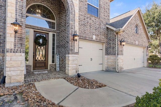 property entrance with concrete driveway, brick siding, a shingled roof, and stone siding