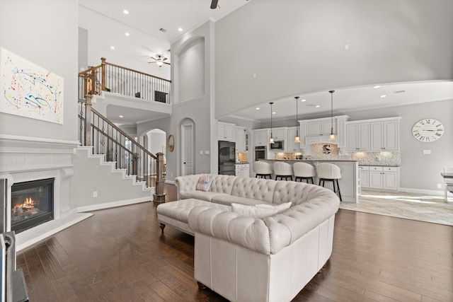 living area with dark wood-style flooring, a towering ceiling, ornamental molding, stairway, and a glass covered fireplace