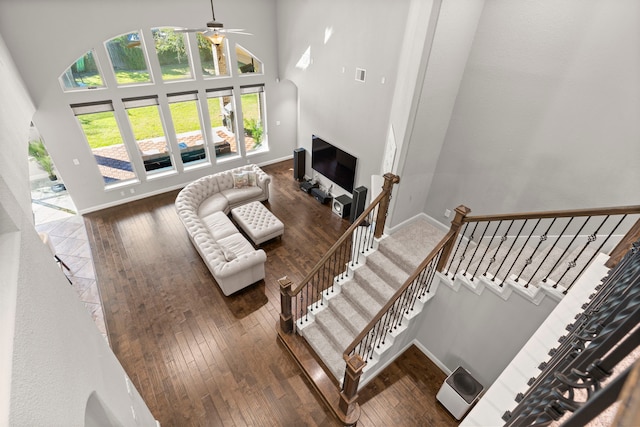 living area featuring visible vents, baseboards, ceiling fan, hardwood / wood-style floors, and a high ceiling