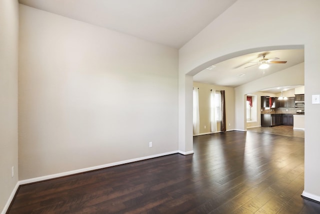 unfurnished living room with baseboards, arched walkways, a ceiling fan, dark wood-style flooring, and vaulted ceiling