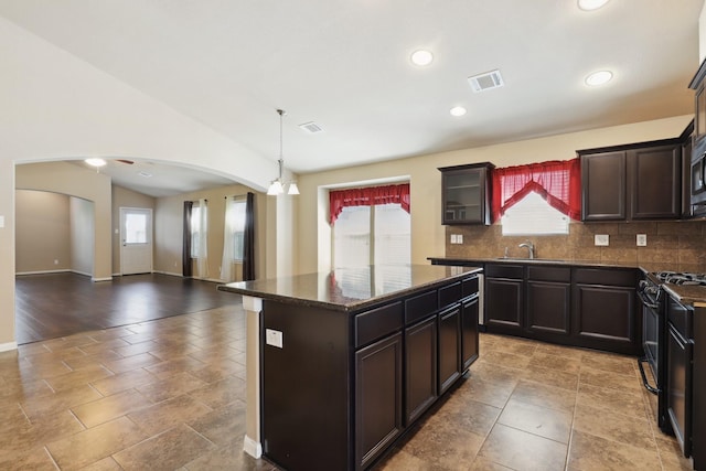 kitchen featuring arched walkways, black gas range, a sink, visible vents, and decorative backsplash