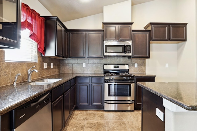 kitchen with lofted ceiling, a sink, appliances with stainless steel finishes, decorative backsplash, and dark stone countertops