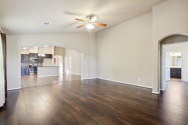 unfurnished living room with ceiling fan, visible vents, arched walkways, and dark wood-style flooring