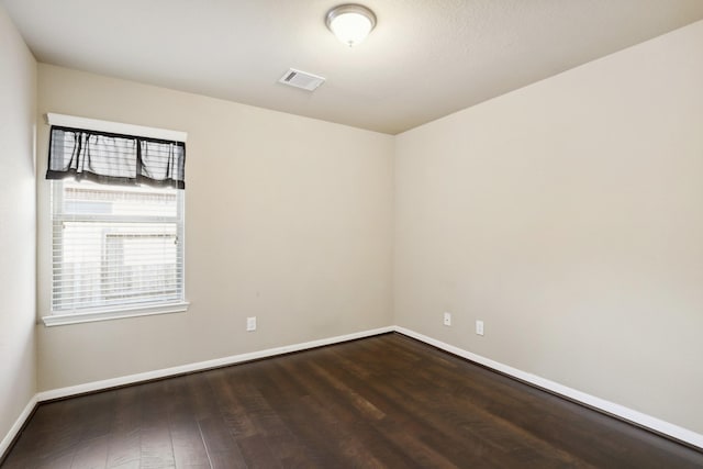 spare room featuring dark wood-type flooring, visible vents, and baseboards