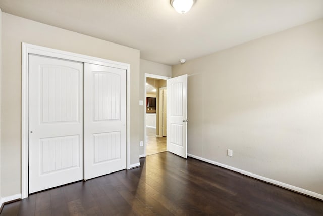 unfurnished bedroom featuring dark wood-style floors, a closet, and baseboards