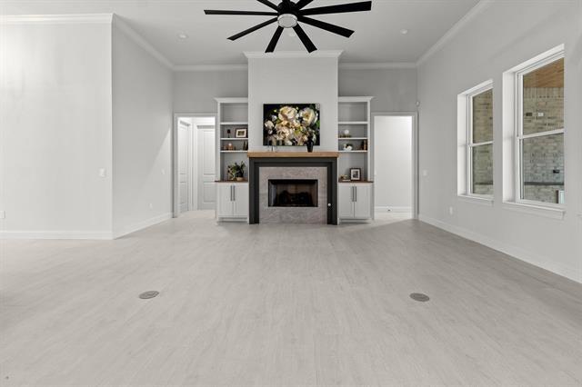 unfurnished living room with baseboards, a tile fireplace, light wood-style flooring, and crown molding