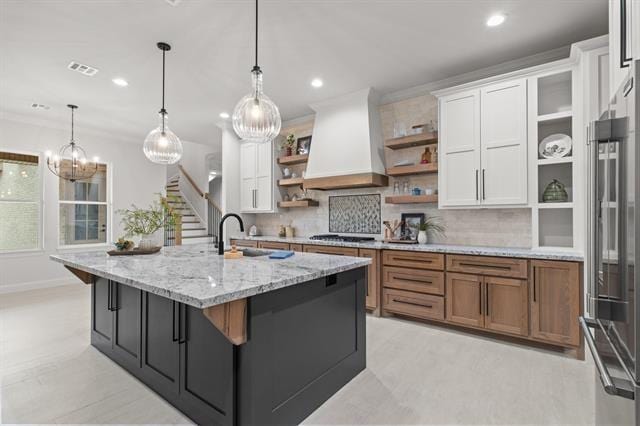 kitchen with tasteful backsplash, premium range hood, white cabinetry, open shelves, and a sink