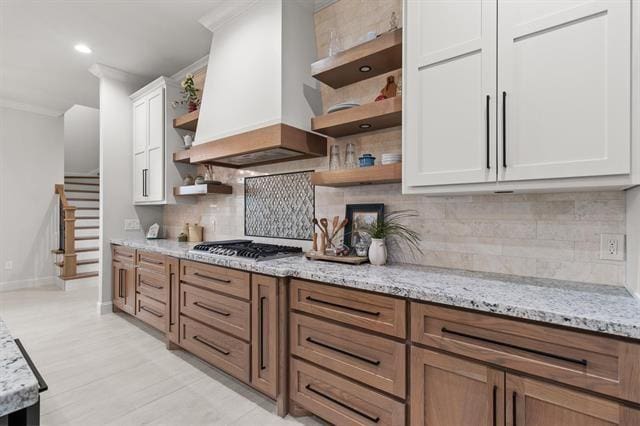 kitchen featuring open shelves, custom range hood, stainless steel gas stovetop, ornamental molding, and white cabinetry