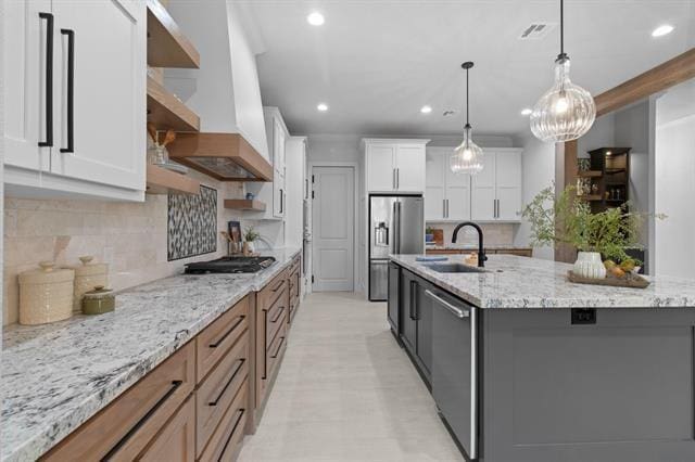 kitchen with open shelves, stainless steel appliances, a spacious island, a sink, and wall chimney range hood