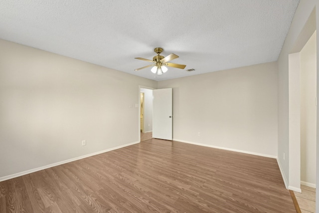 empty room with ceiling fan, a textured ceiling, wood finished floors, visible vents, and baseboards