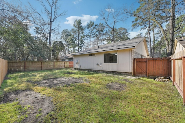 rear view of house featuring a lawn, a fenced backyard, and a gate