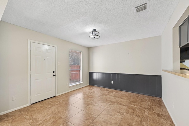 unfurnished room with a textured ceiling, a wainscoted wall, and visible vents