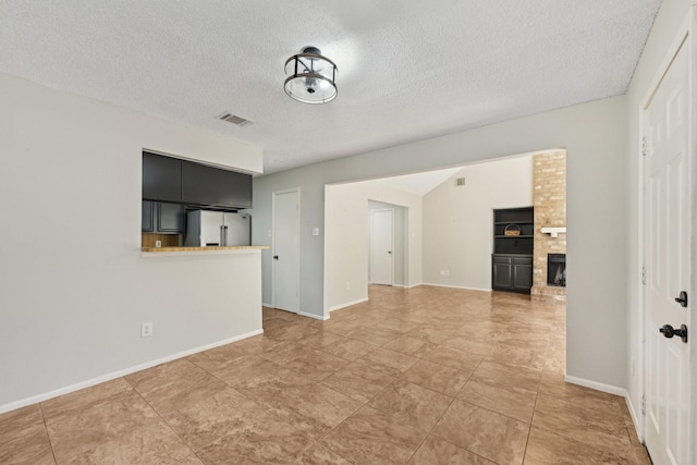 unfurnished living room with a brick fireplace, visible vents, a textured ceiling, and baseboards