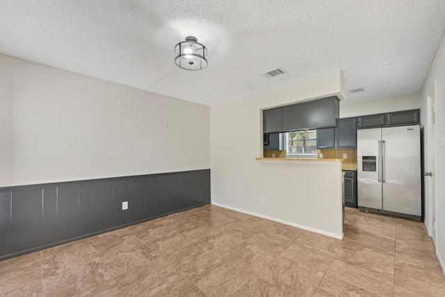 interior space with visible vents, a wainscoted wall, high quality fridge, light countertops, and a textured ceiling