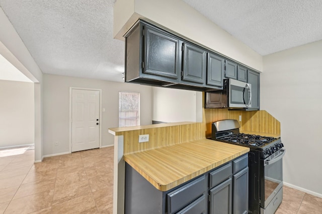 kitchen with a textured ceiling, baseboards, light countertops, stainless steel microwave, and gas stove