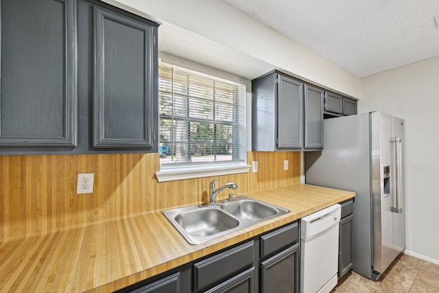 kitchen featuring a textured ceiling, light tile patterned flooring, a sink, wood counters, and dishwasher