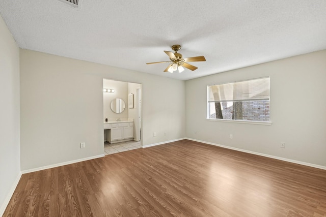 unfurnished bedroom featuring a textured ceiling, ceiling fan, ensuite bathroom, baseboards, and light wood-style floors