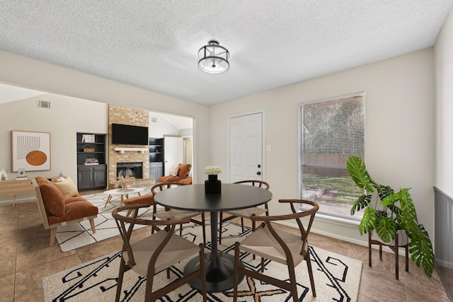 dining space with a fireplace, light tile patterned floors, visible vents, a textured ceiling, and baseboards