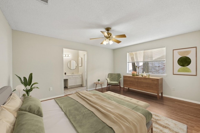 bedroom with baseboards, ensuite bath, a textured ceiling, and light wood finished floors