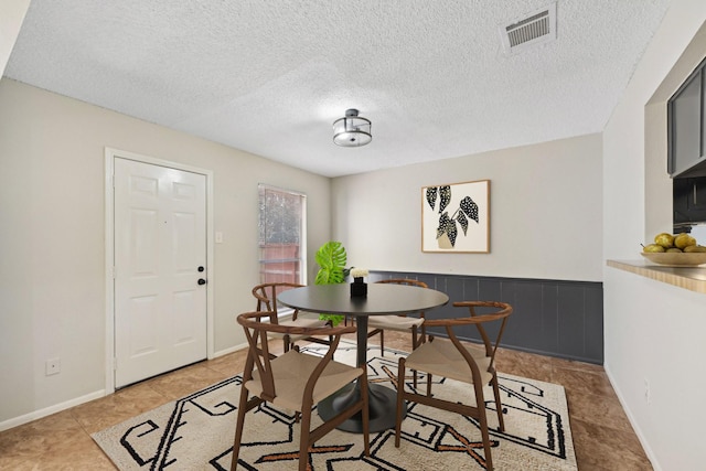 dining space featuring a textured ceiling, a wainscoted wall, and visible vents