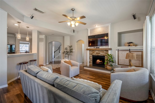 living room featuring visible vents, dark wood-type flooring, ceiling fan, a fireplace, and arched walkways