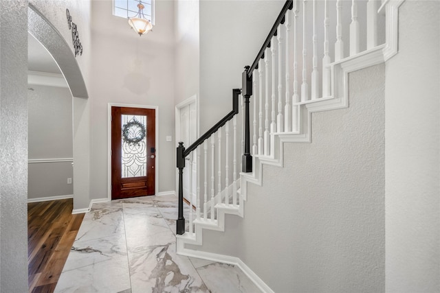 foyer with stairs, baseboards, marble finish floor, and arched walkways