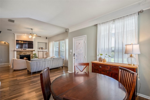 dining room featuring baseboards, visible vents, ceiling fan, a stone fireplace, and dark wood-type flooring