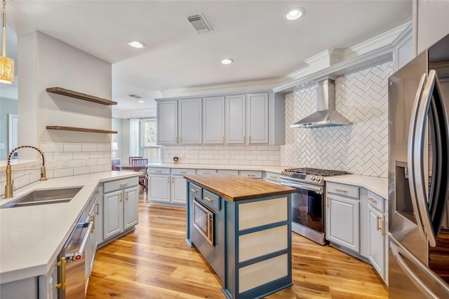 kitchen featuring a sink, wooden counters, stainless steel appliances, wall chimney exhaust hood, and open shelves