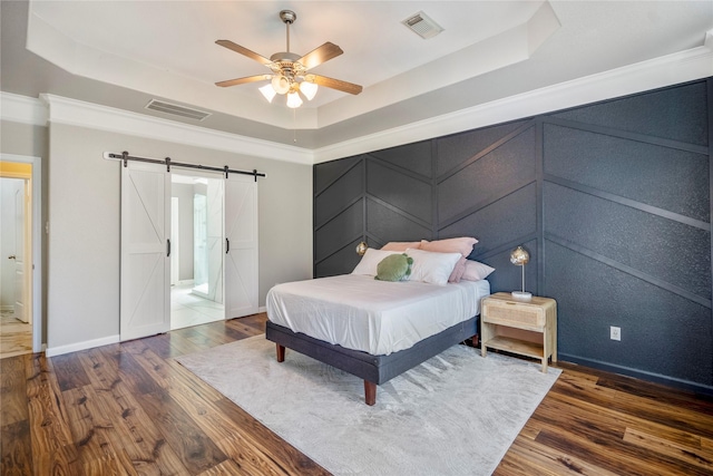 bedroom with visible vents, a raised ceiling, wood finished floors, and a barn door