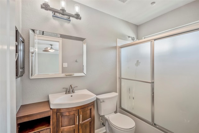 bathroom with toilet, vanity, a textured wall, and shower / bath combination with glass door