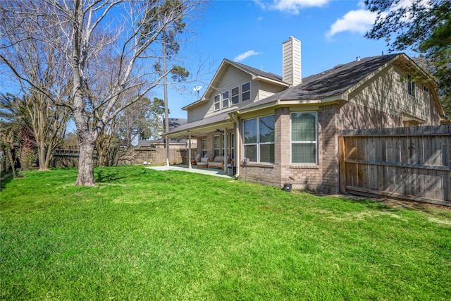 rear view of house with brick siding, a chimney, a yard, a fenced backyard, and a patio area