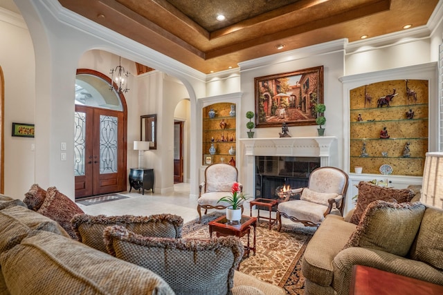 interior space featuring arched walkways, a raised ceiling, a tiled fireplace, ornamental molding, and a chandelier