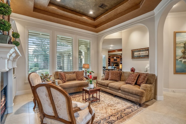 living area with a tray ceiling, arched walkways, crown molding, and a glass covered fireplace