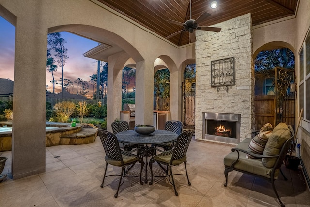 view of patio / terrace featuring outdoor dining area, an outdoor stone fireplace, fence, and a ceiling fan