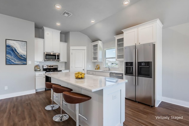 kitchen with stainless steel appliances, a kitchen island, a sink, visible vents, and glass insert cabinets