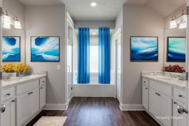 bathroom featuring wood finished floors, two vanities, a sink, baseboards, and a stall shower