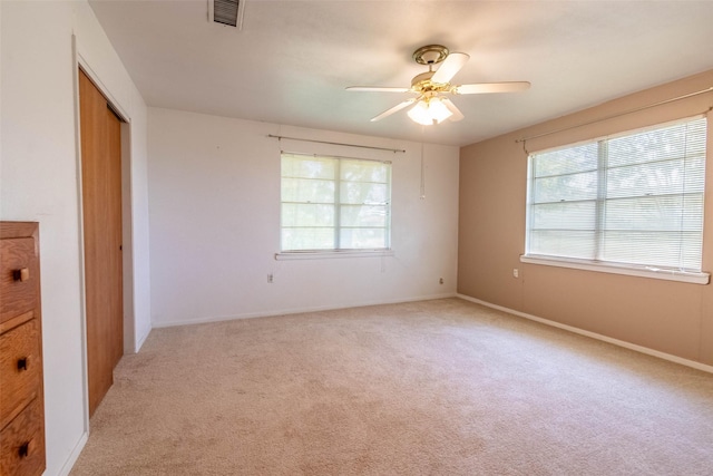 empty room featuring ceiling fan, visible vents, baseboards, and light colored carpet