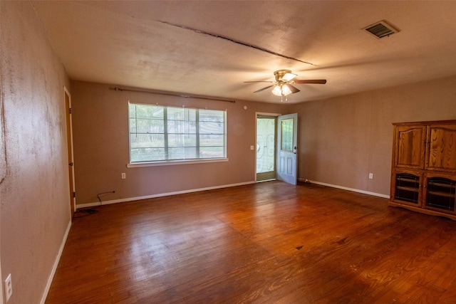 unfurnished living room featuring baseboards, visible vents, ceiling fan, and dark wood-style flooring