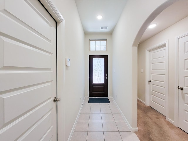 entryway with arched walkways, light tile patterned flooring, visible vents, and baseboards