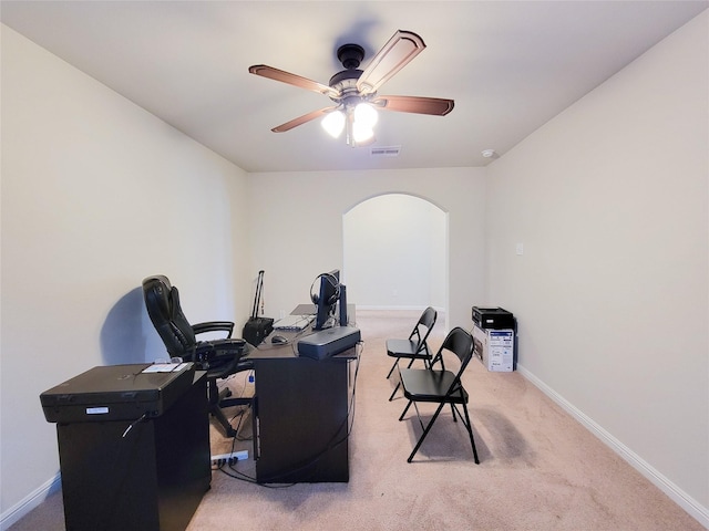 office area with arched walkways, light colored carpet, visible vents, baseboards, and a ceiling fan