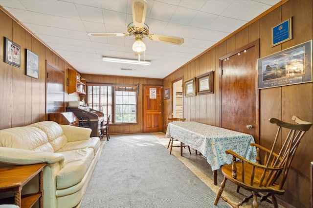 living area featuring carpet, wooden walls, visible vents, and ceiling fan