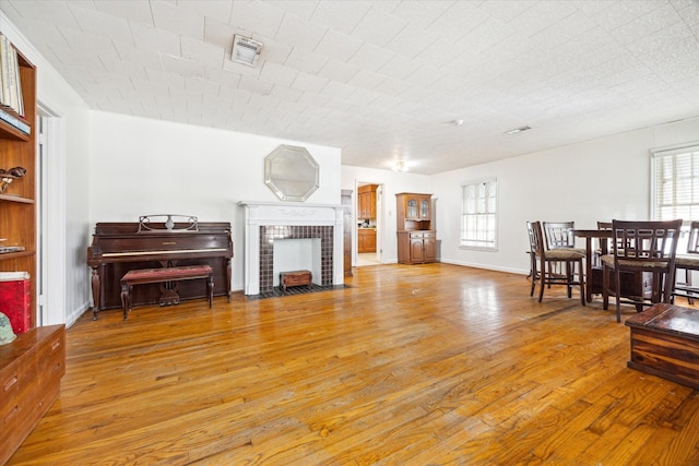 living room featuring a tile fireplace, visible vents, and light wood finished floors