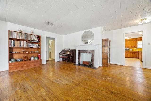 unfurnished living room with wood-type flooring, visible vents, a fireplace, and baseboards