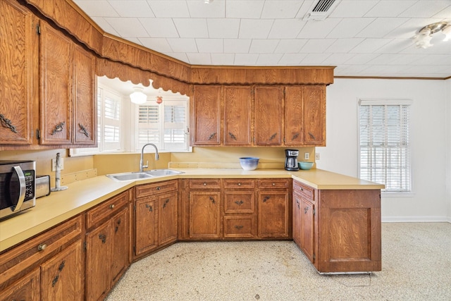 kitchen featuring stainless steel microwave, brown cabinets, a peninsula, light countertops, and a sink