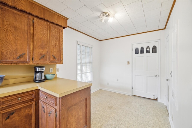 kitchen with a peninsula, baseboards, light countertops, brown cabinets, and crown molding