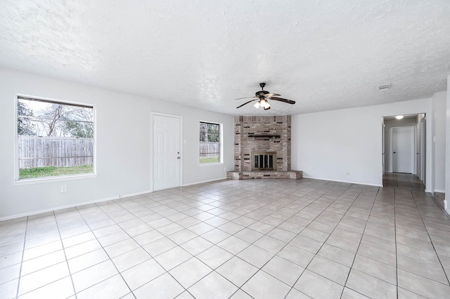 unfurnished living room featuring a fireplace, light tile patterned flooring, ceiling fan, a textured ceiling, and baseboards