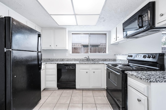 kitchen with light tile patterned floors, white cabinetry, a sink, light stone countertops, and black appliances