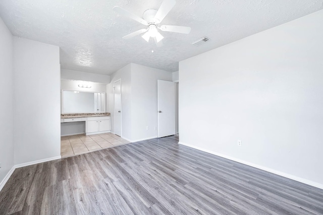 unfurnished living room with a textured ceiling, light wood-type flooring, visible vents, and baseboards